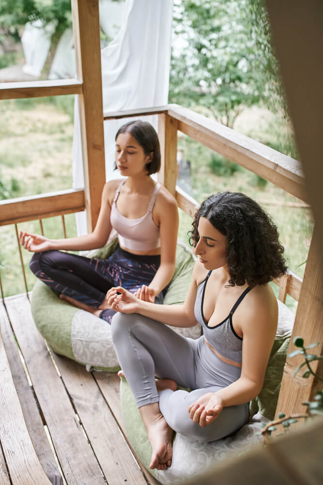 Outdoor Yoga zwei Frauen sitzen auf einer Holzterasse und machen Yoga