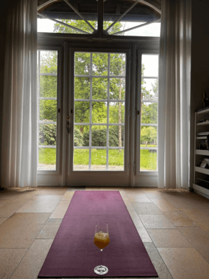 Wein-Yoga Training Eine Yogamatte vor einem Panoramafenster, auf der ein Weinglas steht